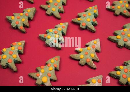 Weihnachtskuchen in Form von Weihnachtsbäumen sind in einem Muster auf einem roten Hintergrund angelegt. Horizontale Ausrichtung Stockfoto