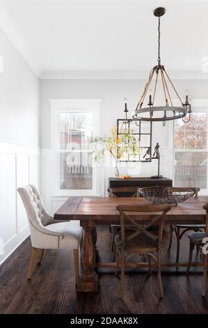 Ein moderner Speisesaal mit rustikalem, bäuerlichem Dekor. Ein großer Holztisch und Stühle sitzen unter einem Kronleuchter aus Eisen und Seil. Stockfoto