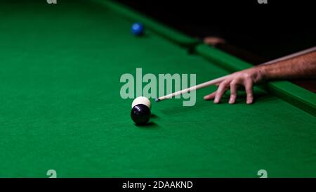 Aufnahme eines Mannes, der Billard spielt. Menschliche Hand mit Queue und Kugeln auf grünem Tuch. Geringer Fokus. Stockfoto