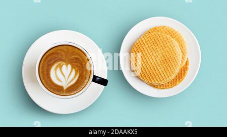 Tasse Kaffee Cappuccino und runde Waffeln in einem weißen Teller auf hellgrünem Hintergrund. Draufsicht. Stockfoto