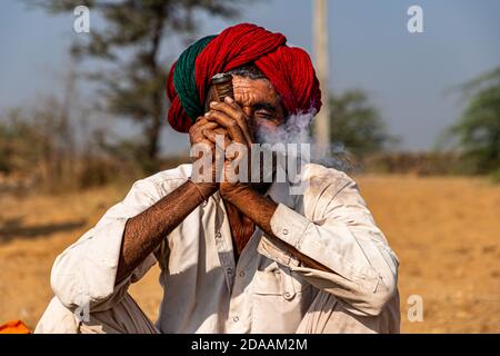 Portrait eines Mannes mit roten traditionellen Turban Rauchen chilam auf pushkar Kamel Festival. Stockfoto