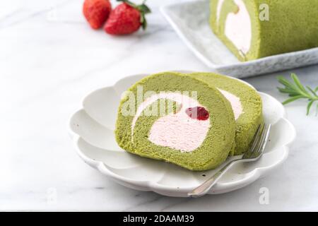 Köstliche Matcha Swiss Roll Cake Scheiben mit Erdbeer-Pudercreme auf weißem Hintergrund, Nahaufnahme. Stockfoto