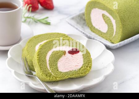 Köstliche Matcha Swiss Roll Cake Scheiben mit Erdbeer-Pudercreme auf weißem Hintergrund, Nahaufnahme. Stockfoto