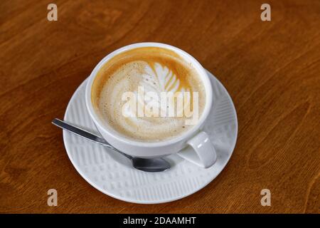 Weiße Tasse Kaffee Cappuccino mit Muster auf Schaumstoffkappe auf braunem Holztisch. Geringer Fokus. Stockfoto