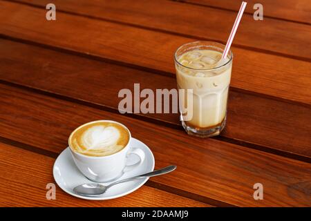 Eine Tasse heißen Cappuccino und ein Glas kalt eislatte auf Holztisch in einem Straßencafé Stockfoto