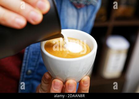 Tasse Cappuccino aus der Nähe im Café. Barista hält und gießt Milch, um Latte Art zu machen. Flacher Fokus. Stockfoto