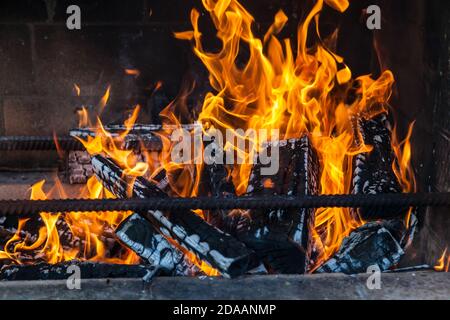 Ein gemauerter, rauchiger Grillofen mit Eisenstangen für Grillspieße mit flammendem Feuer aus verkohlten Holzfeuerhölzern an einem Sommerwochenende im Land Stockfoto