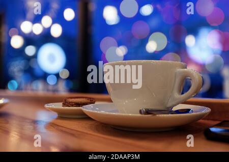 Abend oder Nacht in einem Café. Tasse Kaffee oder Tee auf dem Holztisch vor verschwommenem Hintergrund. Geringer Fokus. Stockfoto