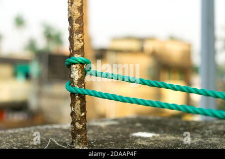 Ein Seil wird in einem Knoten um einen Zaunpfosten gebunden, Seil gebunden Hitch Knoten auf einem rostigen Eisenpol isoliert vom Hintergrund. Stockfoto