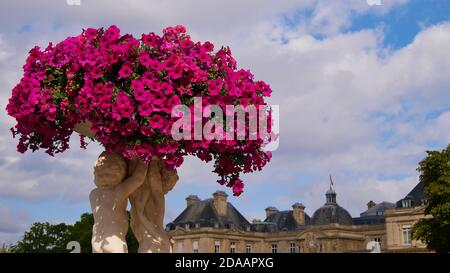 Schöne rosa Blumen auf einer historischen Statue mit alten Luxemburg-Palast (Palais du Luxembourg) im Hintergrund. Stockfoto