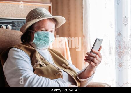 Ältere Frau in Isolation trägt eine medizinische Maske, sprechen auf dem Handy, Videoanruf. Quarantänezeit Stockfoto