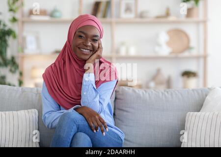 Bescheidene Schwarze Muslimische Frau Im Kopftuch, Die Sich Auf Der Couch Entspannt Zu Hause Stockfoto