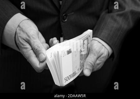 Ein Mann zählt das Geld in einem Geldbündel von 500 Euro. Geringer Fokus. Schwarz-Weiß-Geschäfts- oder Finanzkonzept. Stockfoto