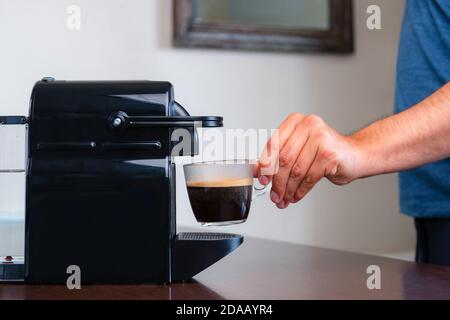 Nahaufnahme der Hand Abholung einer Tasse Espresso Kapsel Kaffeemaschine zu Hause. Konzept der Kaffeepause. Stockfoto