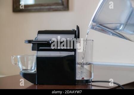 Nahaufnahme der Hand Gießen reines gefiltertes Wasser in Kapsel Kaffeemaschine. Stockfoto