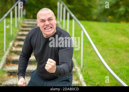Wütender Mann, der die Kamera mit der Faust bedroht Schreit Missbrauch mit einem heftigen Ausdruck auf draußen tritt in Ein Park Stockfoto