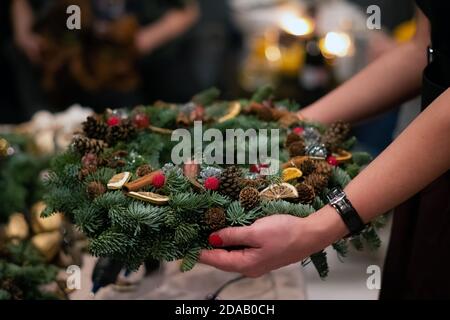 Weihnachten Kranz Weberei. Frau Hände verzieren holiday Wreath der Fichte Äste, Kegel und verschiedenen organischen Dekorationen auf dem Tisch Stockfoto