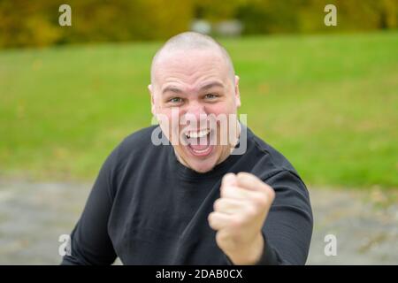 Aggressiv drohende wütend jungen Mann schreien an die Kamera als Er schlägt mit der Faust im Freien in einem Park Stockfoto