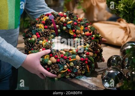 Person hält schöne und bunte Hand gemacht Weihnachtskranz, grüne Fichtenzweige mit Tannenzapfen und andere Dekorationen dekoriert. Weihnachtslch Stockfoto