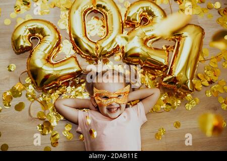 Mädchen in einer Maske mit den Zahlen 2021 freut sich Bei Konfetti fliegen von oben Stockfoto