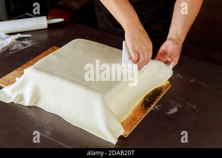Frau Dekoration quadratischen Kuchen mit weißen Fondant. Technik der Herstellung Hochzeitstorte. Stockfoto