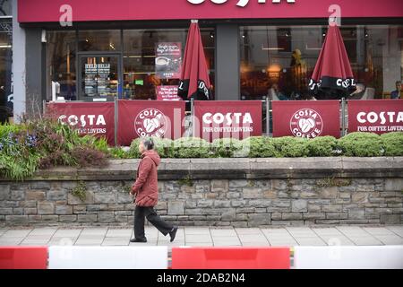 Eine Person geht an der Außenseite eines Costa Costa-Outlet in Großbritannien vorbei. Der Sitzbereich im Freien ist zu sehen und die Beschilderung ist zu sehen. Stockfoto