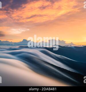 Erstaunlicher fließender Morgennebel in den Frühlingsbergen verschwommen von langer Belichtung. Schöner Sonnenaufgang im Hintergrund. Landschaftsfotografie Stockfoto