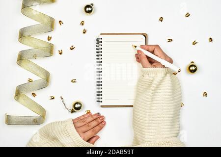 Schreiben eines Briefes an Santa Clause. Frau, die neue Jahr-Resolutionen auf Notizblock schreibt. Heller Arbeitsbereich mit Weihnachtsdekorationen. Weibliche Hand schreiben auf Stockfoto