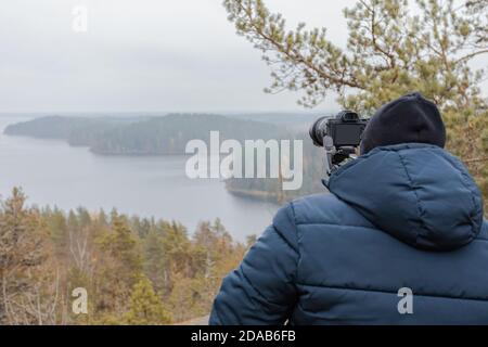 Mann fotografiert Herbstlandschaft vom Berg durch Wälder und Seen bei bewölktem Wetter und Nebel. Rock Hiidenvuori. Finnland. Hochwertige Fotos Stockfoto