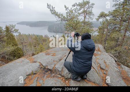 Mann fotografiert Herbstlandschaft vom Berg durch Wälder und Seen bei bewölktem Wetter und Nebel. Rock Hiidenvuori. Finnland. Hochwertige Fotos Stockfoto