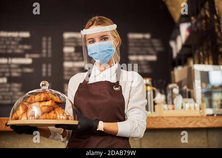 Hübsche Kellnerin, die während einer Pandemie ein Tablett mit Gebäck im Café trug Stockfoto