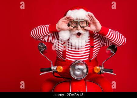 Foto von funky Rentner alten Mann Moped Fahrt offenen Mund Halten Sie Brillen unglaubliche Geschwindigkeit Wind tragen weihnachtsmann x-Mas Kostüm Hosenträger Sonnenschutzstiefel gestreift Stockfoto