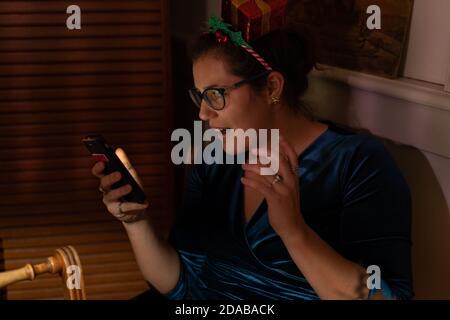 Erstaunt junge Frau mit weihnachten Haar Dekor Blick in ihr Telefon zu weihnachten. Stockfoto