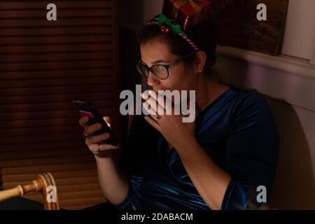 Erstaunt junge Frau mit weihnachten Haar Dekor Blick in ihr Telefon zu weihnachten. Stockfoto