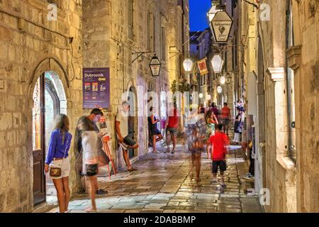 Nachtszene entlang einer schmalen Straße in der Altstadt von Dubrovnik, Kroatien, voll mit Touristen, die herumschlendern und die kleinen Boutiquen erkunden. Stockfoto