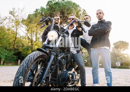 Drei Männer stehen neben einem Biker auf einem von Bäumen umgebenen Parkplatz. Freundschaft und Teamkonzept Stockfoto