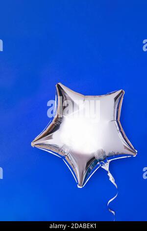 Ein silberner Glitter-Folienballon in Sternform auf Blau Stockfoto