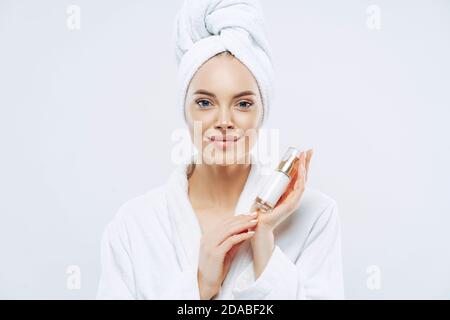 Calm wunderschöne Frau mit gesunder Haut hält Flasche Schönheit Körperlotion für die Pflege, Posen in Bademantel nach der Dusche, wirbt kosmetische prodcut Stockfoto