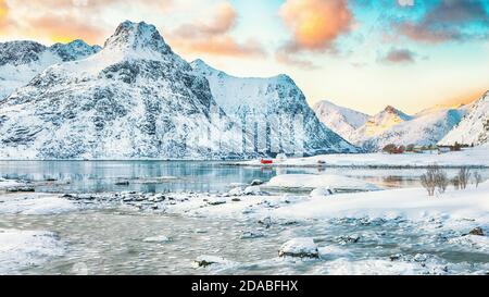 Gefrorene Flakstadpollen und Boosen Fjorde mit roten Rorbuern und Reflexion im Wasser bei Sonnenaufgang mit Hustinden Berg im Hintergrund. Lage: Flak Stockfoto