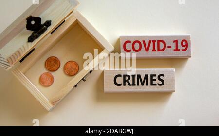 Konzeptworte 'COVID-19 Crimes' auf Blöcken auf einem schönen weißen Hintergrund, kleine Truhe mit Münzen. Schöner weißer Hintergrund, Kopierbereich. Unternehmen und Stockfoto