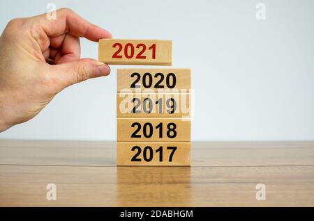 Männliche Hand, die einen Block mit der Nummer '2021' auf einen Turm mit den Nummern '2017, 2018, 2019, 2020' setzt. Schöner Holztisch, weißer Hintergrund. Kopie en Stockfoto