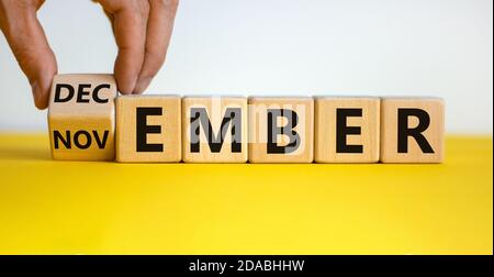 Symbol für den Wechsel von November auf Dezember. Männliche Hand falzt Holzwürfel und ändert die Aufschrift 'november' in 'Dezember'. Schöne gelbe t Stockfoto