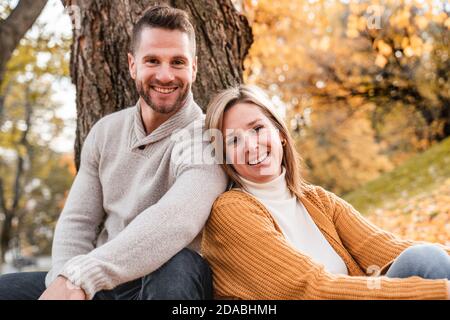 Liebevolles Paar im Herbstpark sitzt auf dem Boden Eines Baumes Stockfoto