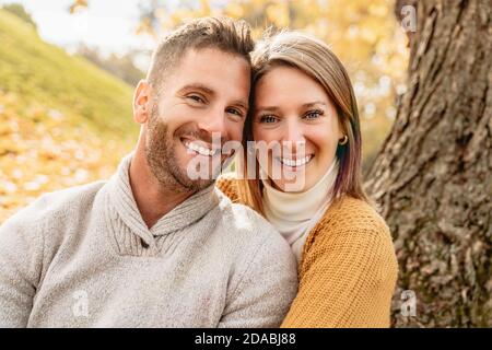 Liebevolles Paar im Herbstpark sitzt auf dem Boden Eines Baumes Stockfoto