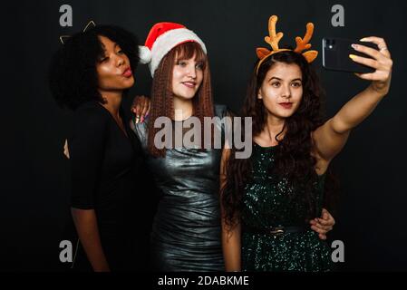 Gruppe von Freunden im Club machen Selfie und Spaß haben. Nette junge Frauen posieren mit küssen Gesichtsausdruck. Entspannte junge Frauen machen Selfie mit Freund auf dunklem Hintergrund während der weihnachtsfeier. Stockfoto