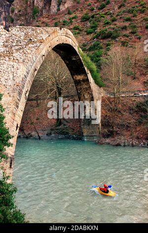 Kajak auf Aoos Fluss, unter der alten Steinbogenbrücke von Konitsa, Ioannina, Epirus, Griechenland. Stockfoto