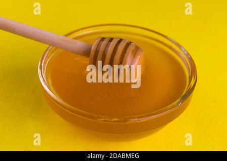 Honig in einer Glasschale fließt auf gelbem Hintergrund den Honigstab hinunter. Nahaufnahme. Stockfoto