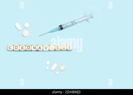 Coronavirus Wort mit Holzbuchstabenwürfel auf einem Licht gemacht Blauer Hintergrund mit einer Spritze Stockfoto