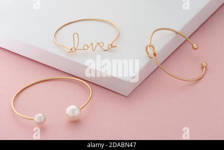 Drei moderne goldene Armbänder auf weißem und rosa Farben Hintergrund Stockfoto