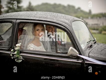 Glückliches Paar kurz vor der Hochzeit im klassischen VW Käfer an einem regnerischen Tag in Polen. Stockfoto